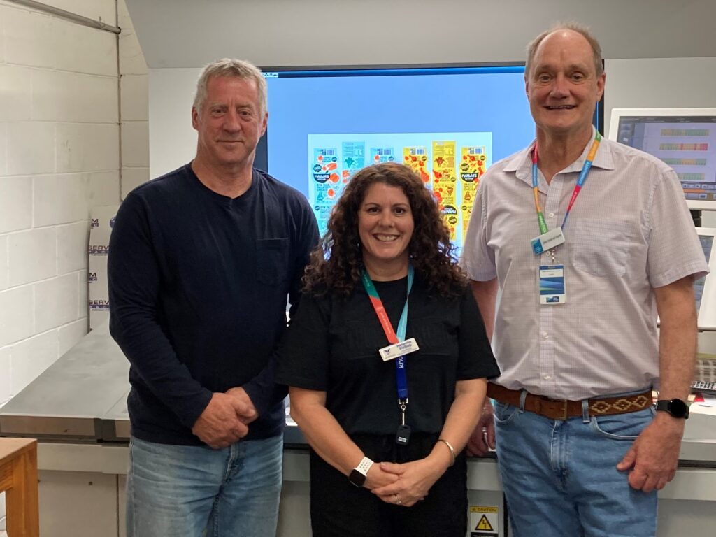 An image of three people standing in front of a printing machine