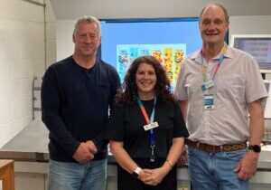 An image of three people standing in front of a printing machine